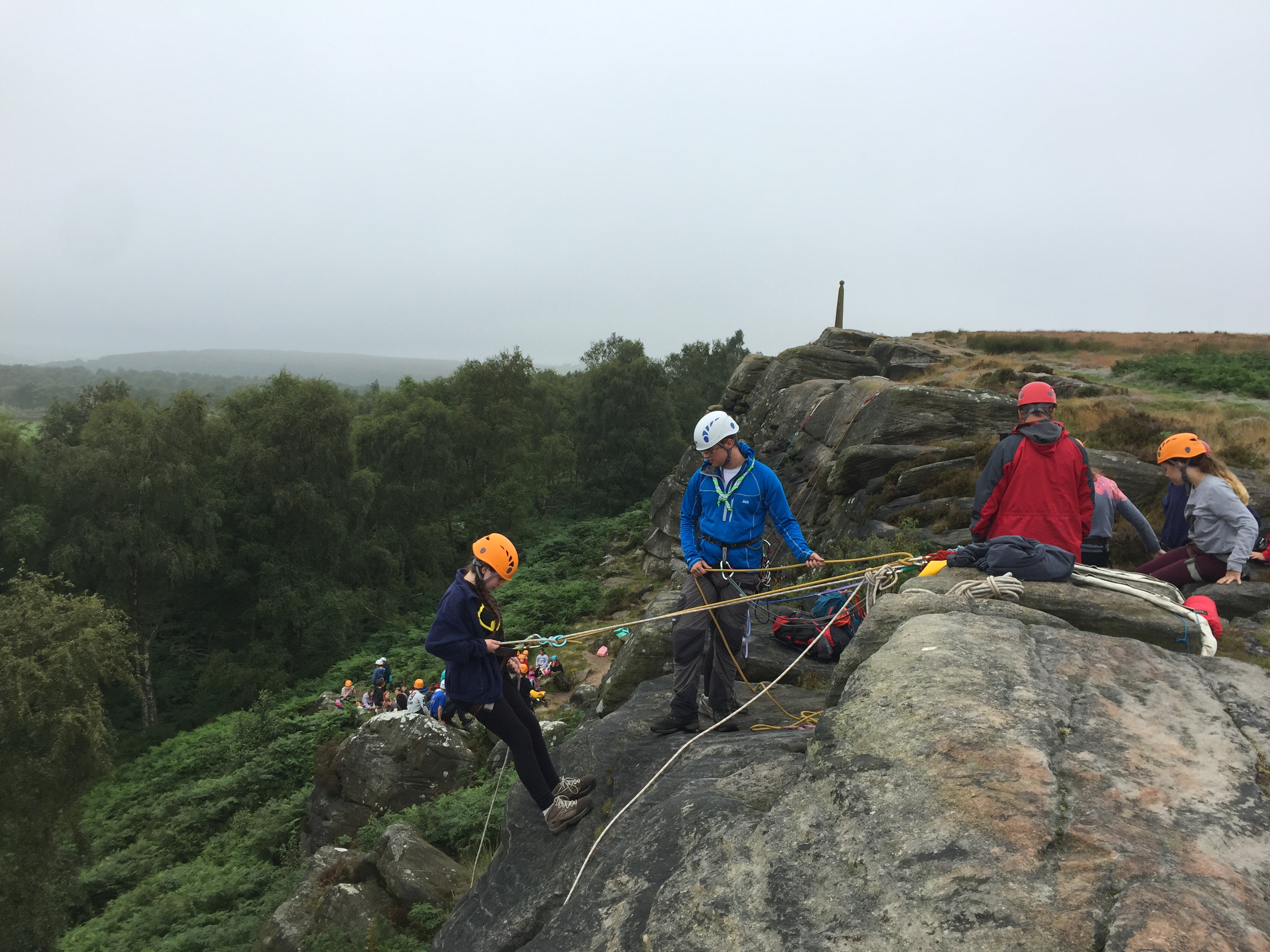 A group abseiling from some rocks, with some trees in the background.