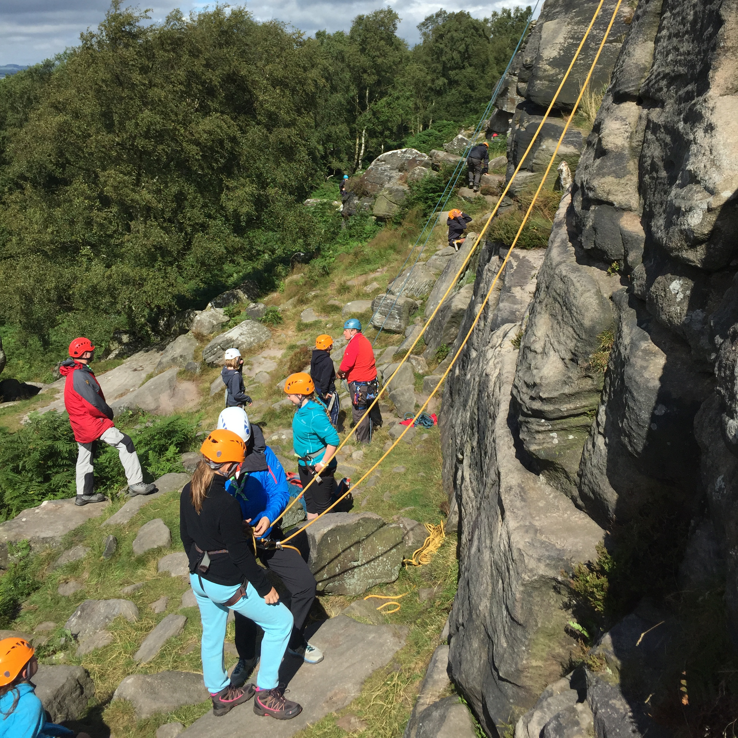 A group of young people climbing at a crag of rough ledges.