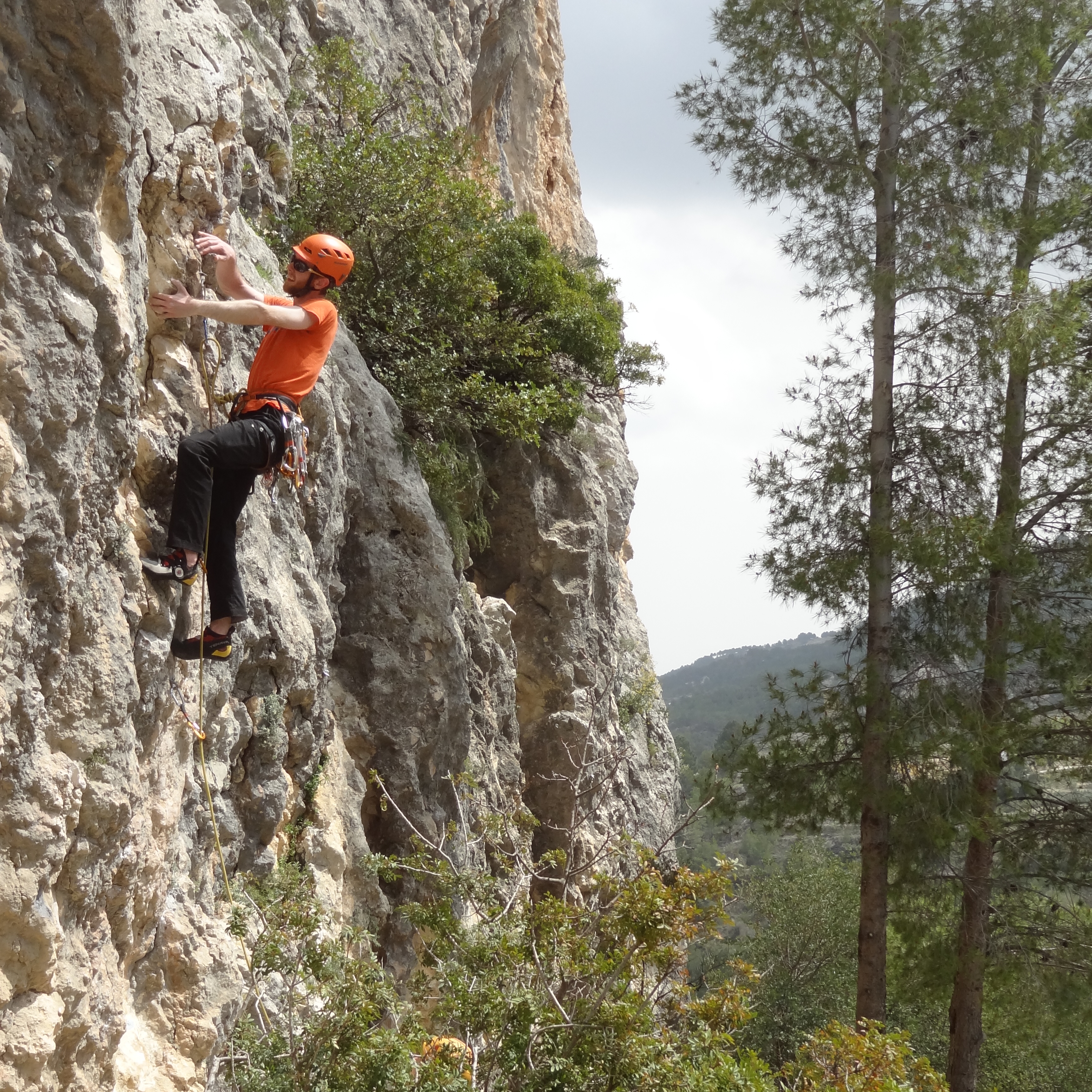 Phill wearing an orange shirt and helmet, climbing a vertical wall.