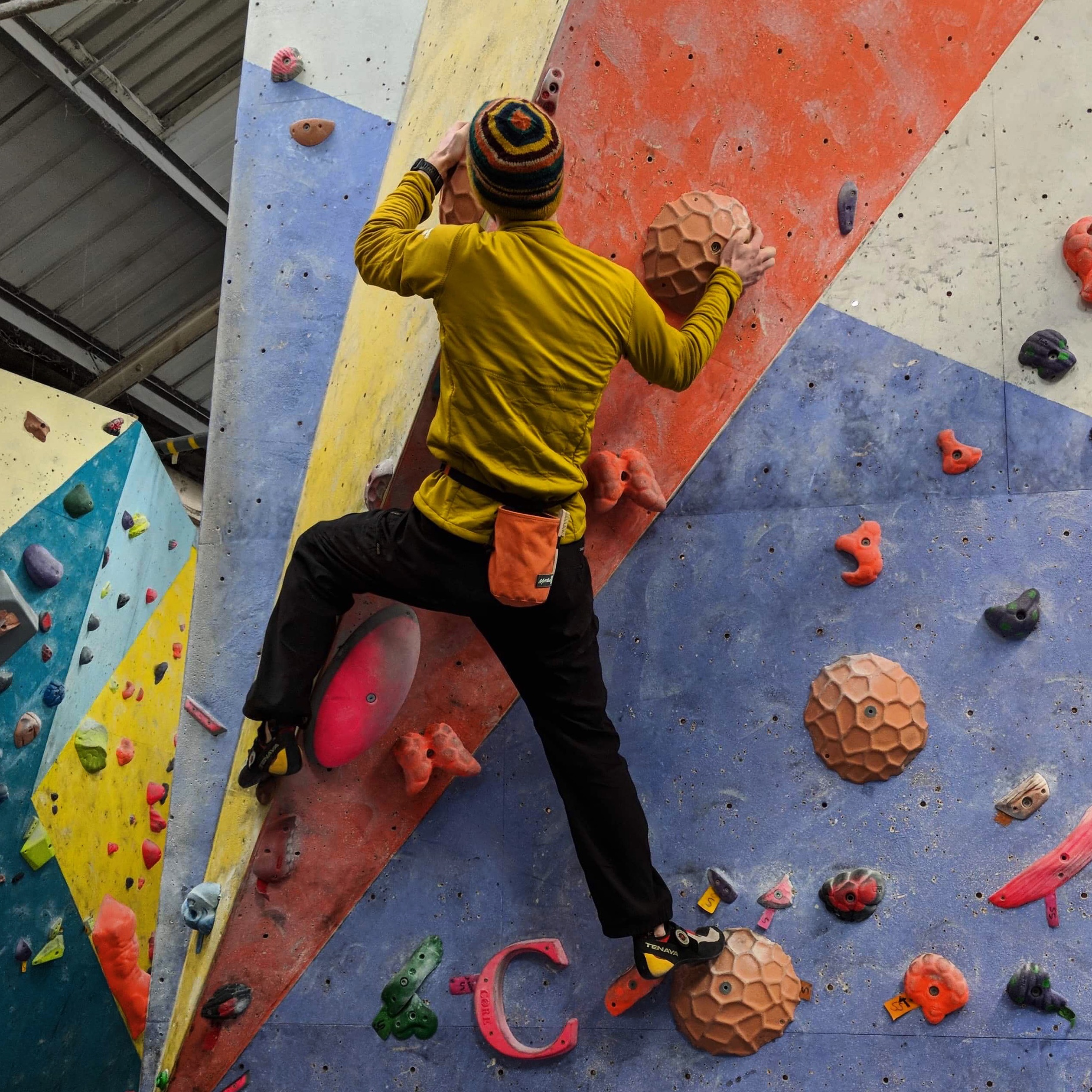 Phill wearing a yellow top, climbing on a multi-coloured bouldering wall.