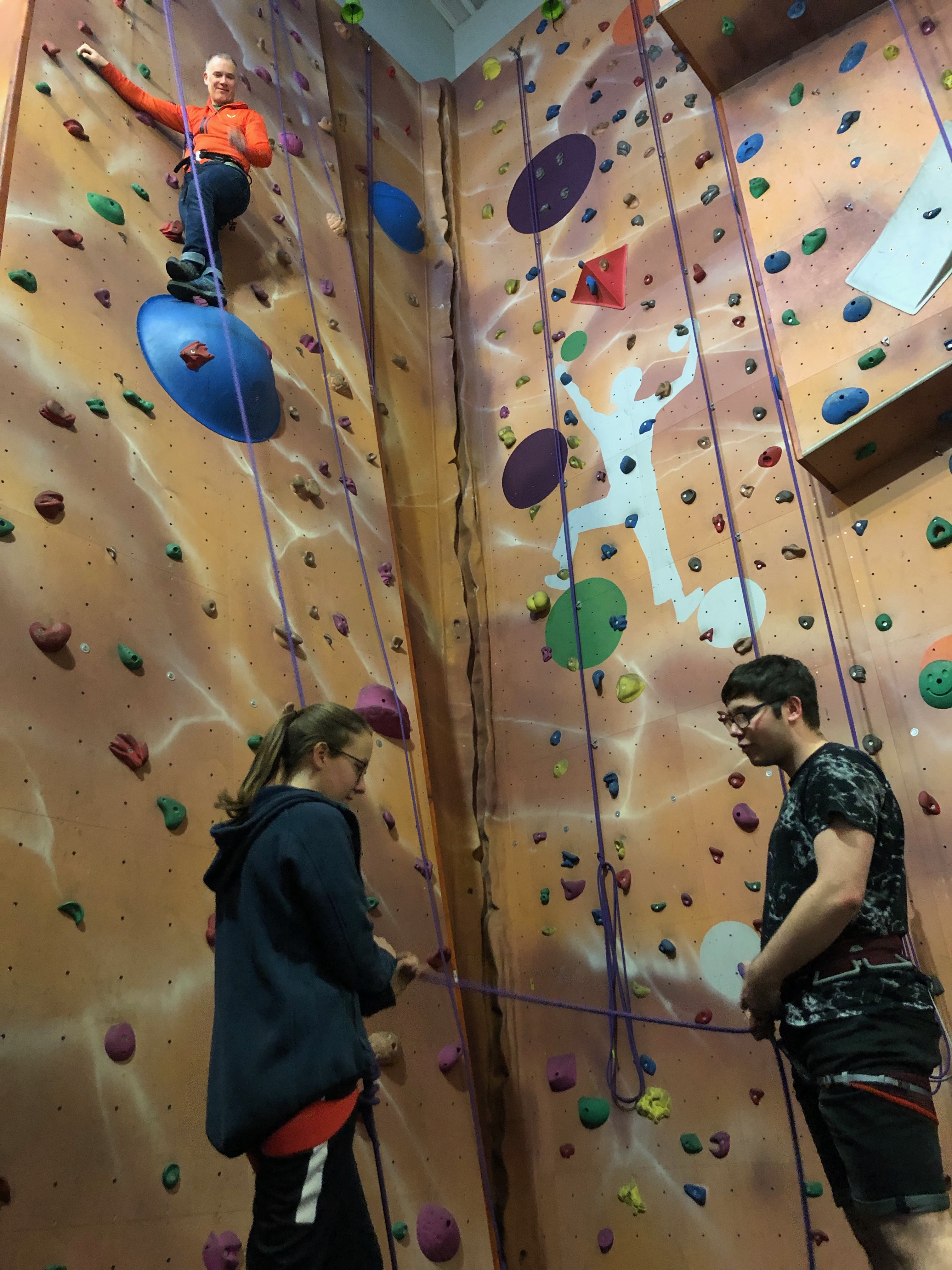 A climber is stood on a large, round, blue volume at the top of the wall.