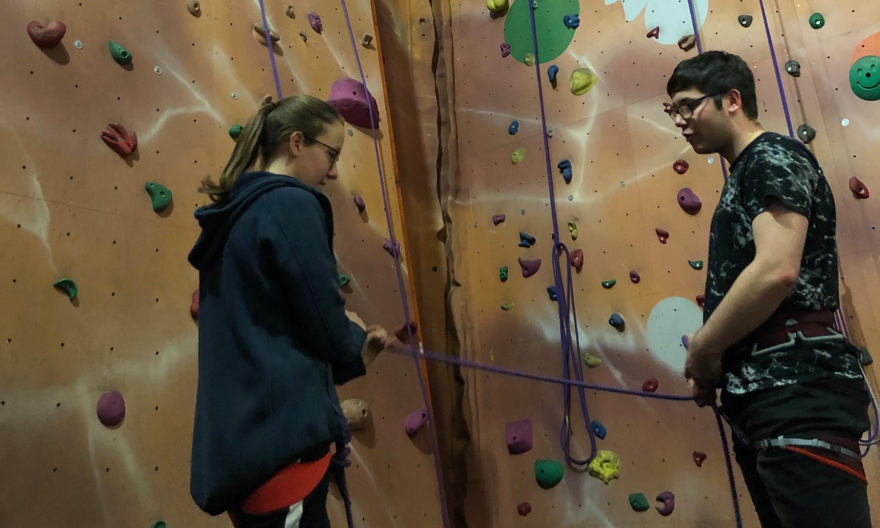 A young person learning to belay with an assistant holding their rope.